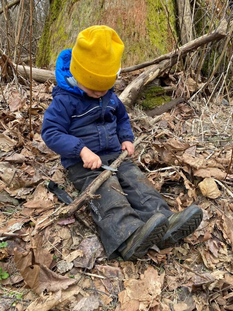 3歳ほどの男の子が地面に座りナイフを使うようす